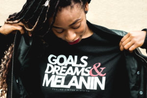 A girl wears a t-shirt that says Goals Dreams and Melanin