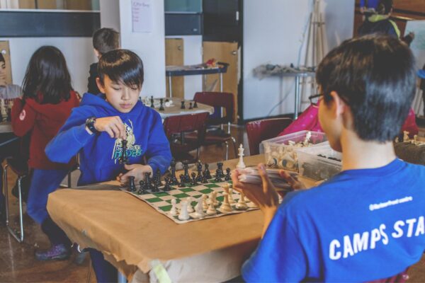 Kid playing chess with Camps Staff