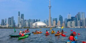 A group of children kayaking on the Toronto waterfront with the CN tower in the background