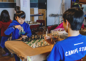 Kid playing chess with Camps Staff