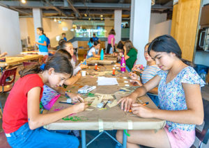A group of kids working on their designs at a long table
