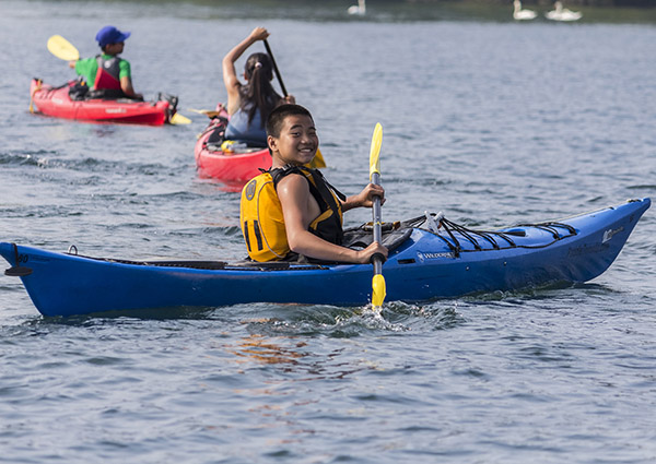 Smiling kid paddles their kayak on the water