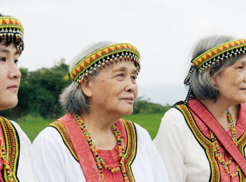 Three Asian women wearing traditional attire looking at a distance outdoors.