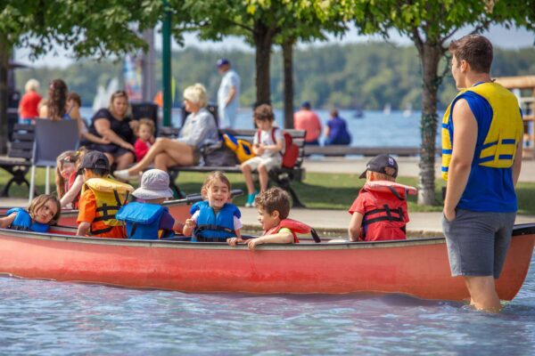 A canoe instructor with a group of kids on a lake outside.