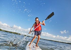 Young boy standing on a stand up paddleboard in the water during the summer
