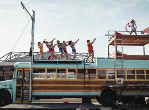 Group of performers standing on a school bus holding hula hoops and dancing.