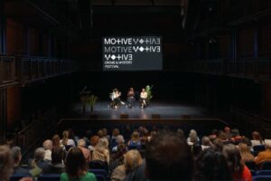 Audience watches a book panel event inside a dark theatre.
