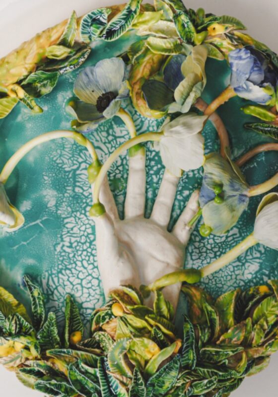 A ceramic platter with plants along its border and a hand at its centre. Flowers are growing out of the hand.