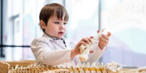 A little kid playing with pretend health science tools wearing a pretend lab coat