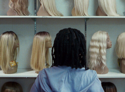 A young child standing looking at a shelf of mannequins facing away from the camera.