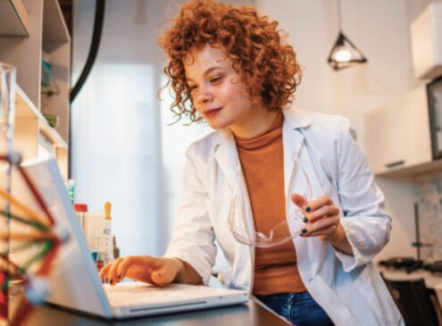 Young girl with curly red hair wearing a lab coat browsing on a laptop.