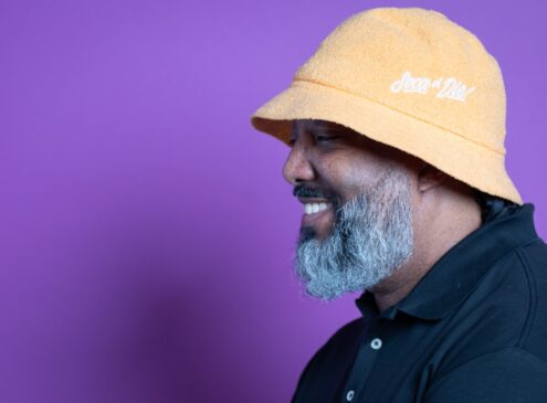 A man wearing a yellow hat against a purple background.