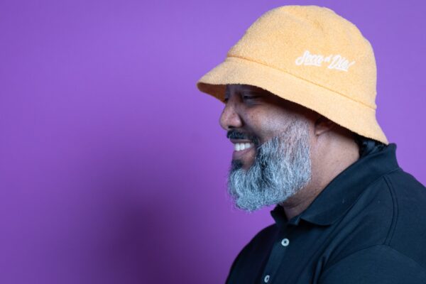 A man wearing a yellow hat against a purple background.