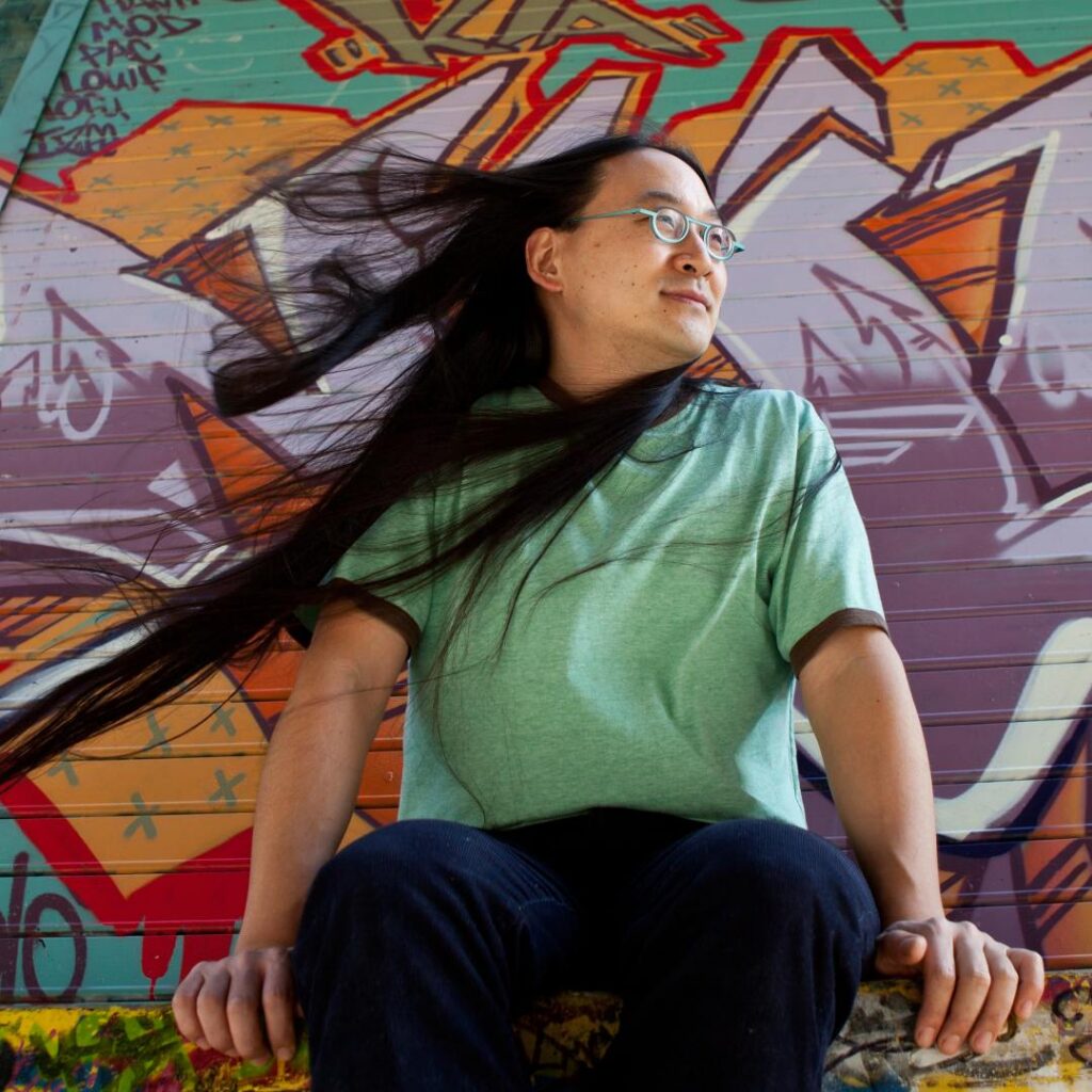 A person sitting with his hair blowing in the wind against a graffiti wall