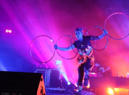 Artist holding hoops dancing against a colourful background.