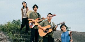 Group of four musicians posing outdoors with their instruments.