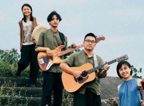 Group of four musicians posing outdoors with their instruments.