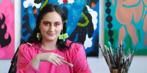 A woman wearing a bright pink shirt holding a paintbrush posing for the camera