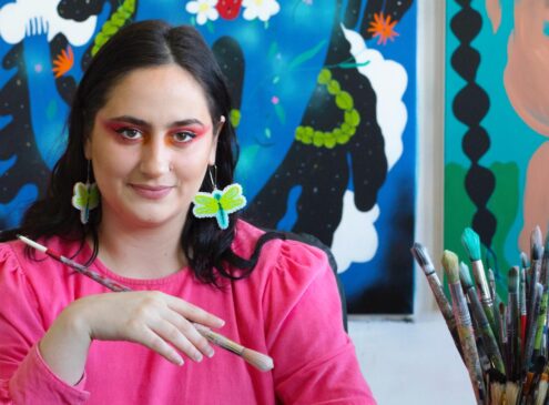 A woman wearing a bright pink shirt holding a paintbrush posing for the camera