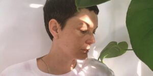 A close-up image of a woman posing by a plant