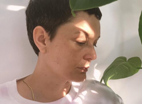 A close-up image of a woman posing by a plant