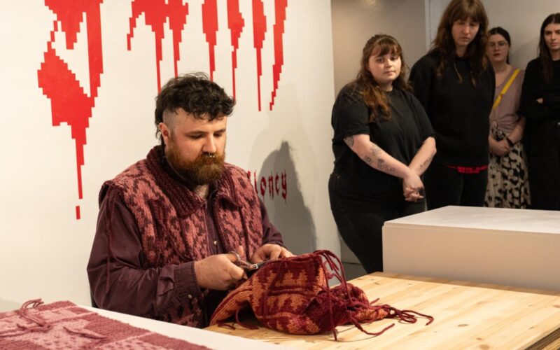 A man working on a red textile piece in a room