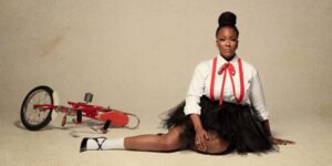 A woman posing for the camera sitting on the floor next to a bicycle