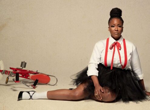 A woman posing for the camera sitting on the floor next to a bicycle