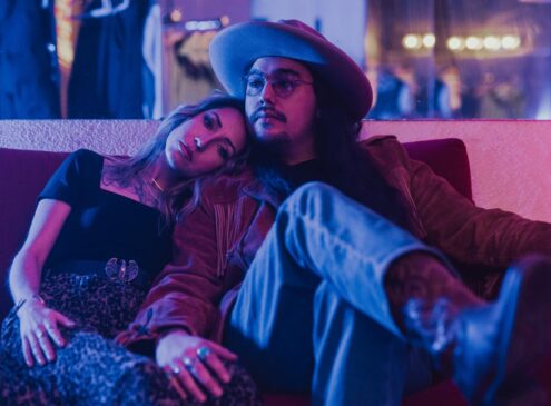 A couple sit on a couch posing for the camera against blue light
