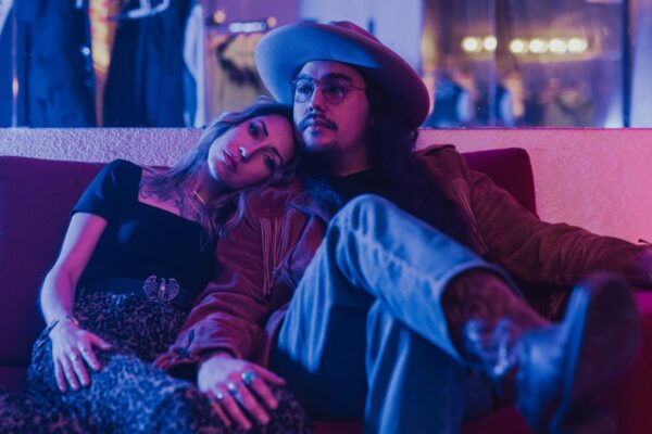 A couple sit on a couch posing for the camera against blue light