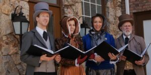 A group of four carolers wearing period attire holding books and singing