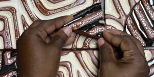 Up-close shot of two hands working with patterned ceramic tiles.
