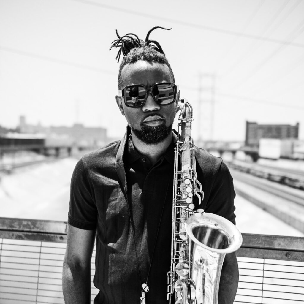 A black and white image of a man holding a saxophone outside