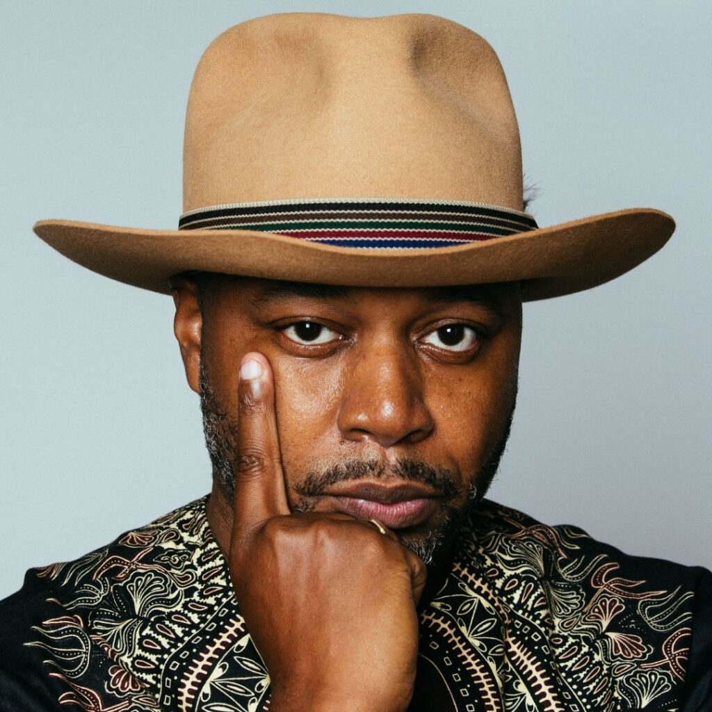 A man wearing a hat holding up a finger and posing for the camera