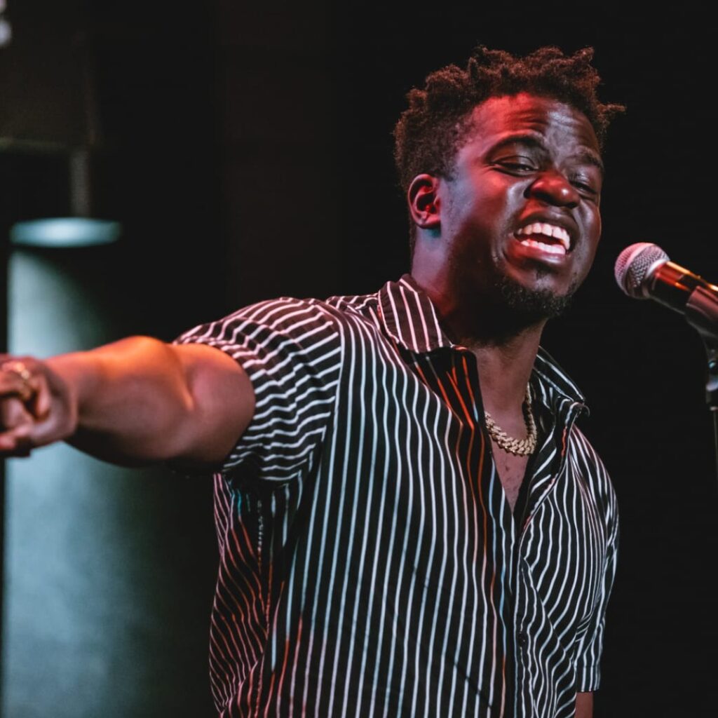 A man wearing a striped shirt performing on stage with a mic