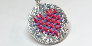 A close-up of an embroidered silver pendant