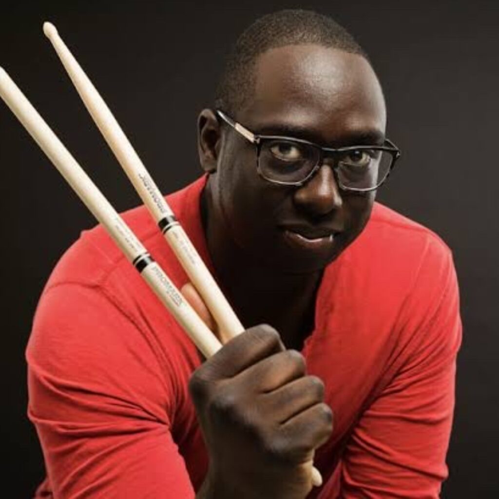 A man wearing a red shirt holding drum sticks