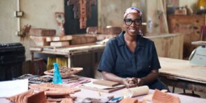 A woman wearing a headscarf sitting down with her artwork in a studio