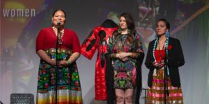 Three women wearing red attire on stage talking