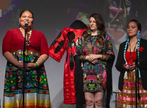 Three women wearing red attire on stage talking