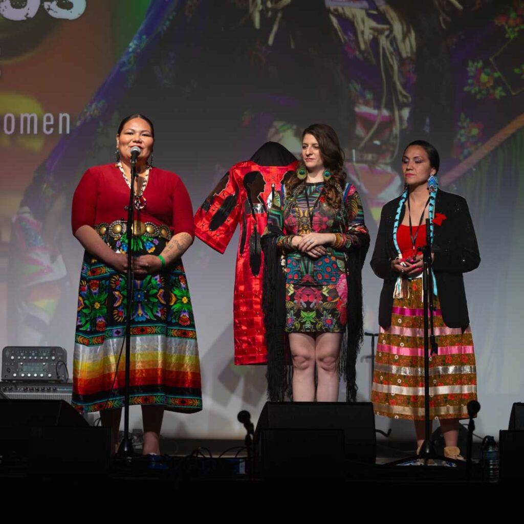 A group of three woman wearing colourful clothing on stage