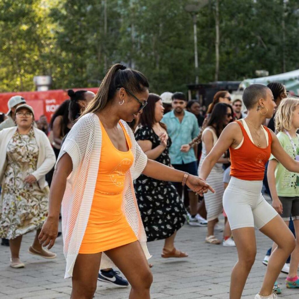 A woman wearing a bright orange dress teaching a dance class outside