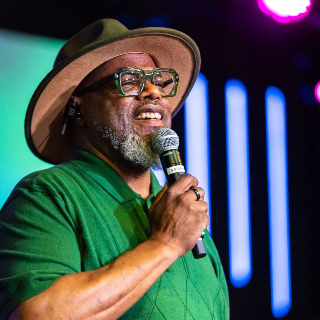 A man wearing a bright green shirt and hat holding a mic on stage