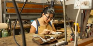 A woman working on a pendant jewellery piece in a metal studio