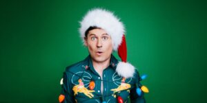 A man wearing a Santa hat covered in holiday lights against a green background