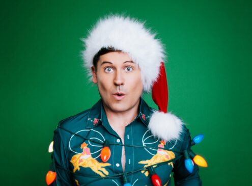 A man wearing a Santa hat covered in holiday lights against a green background