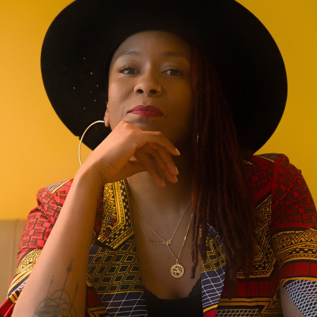 A woman wearing a black hat posing for the camera against a yellow background