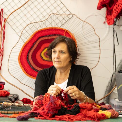 A woman holding red embroidered textiles sitting in a studio
