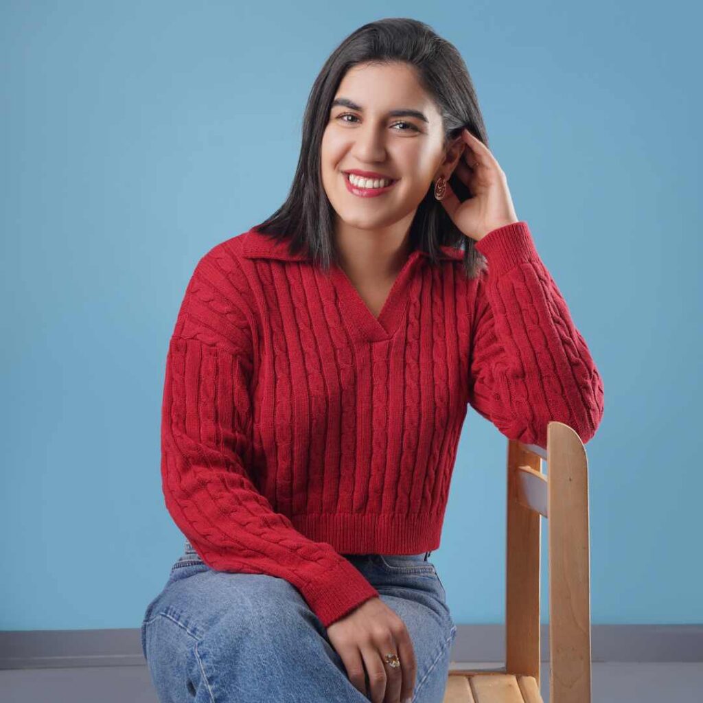 A woman wearing a red sweater posing and smiling while sitting on a chair