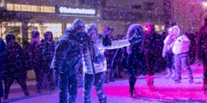 A crowd skating at an outdoor rink at night while it's snowing